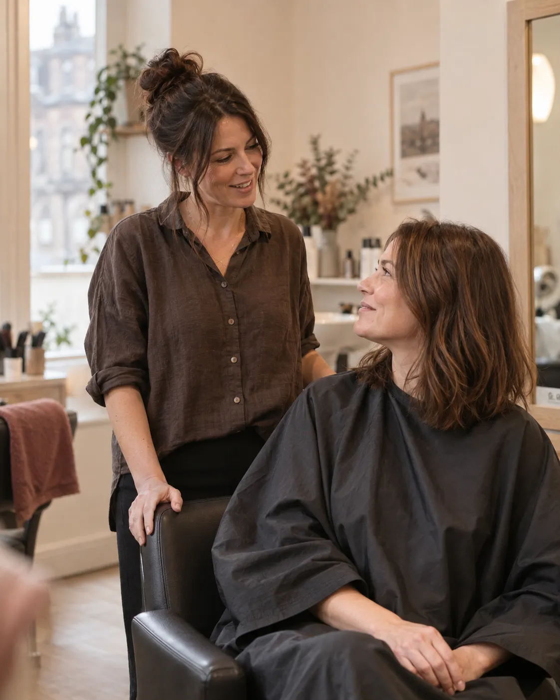 A relaxed hair consultation between a stylist and client in a softly lit salon.